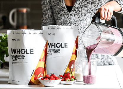 Vivo Life Whole Plant-Based Nutritional Shake supplement in a glass with a scoop of powder and fresh ingredients around it.